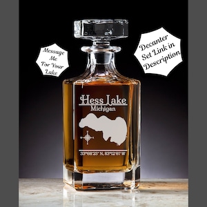 May include: A clear glass decanter with a square base and a stopper. The decanter is engraved with the words "Hess Lake Michigan" and the coordinates "33°08′25″ N, 83°12′07 W".
