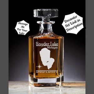 May include: A clear glass decanter with a square base and a stopper. The decanter is engraved with the words "Snyder Lake, Michigan" and the coordinates "44°50′23″ N, 84°19'11" W".