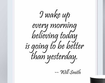 Könnte beinhalten: Gerahmter Druck mit dem Zitat „Ich wache jeden Morgen auf und glaube, dass der heutige Tag besser wird als gestern.“ von Will Smith. Eine schwarze Tasse, ein durchsichtiger Glaskerzenhalter und eine Schale mit Orangen stehen ebenfalls auf der weißen Oberfläche.