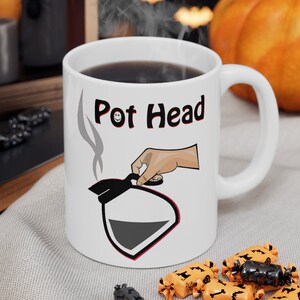 May include: White ceramic coffee mug with a black and red illustration of a coffee pot and the text "Pot Head".