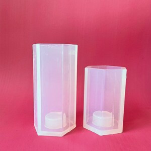May include: Two clear plastic hexagonal candle molds. The larger mold is taller than the smaller mold.