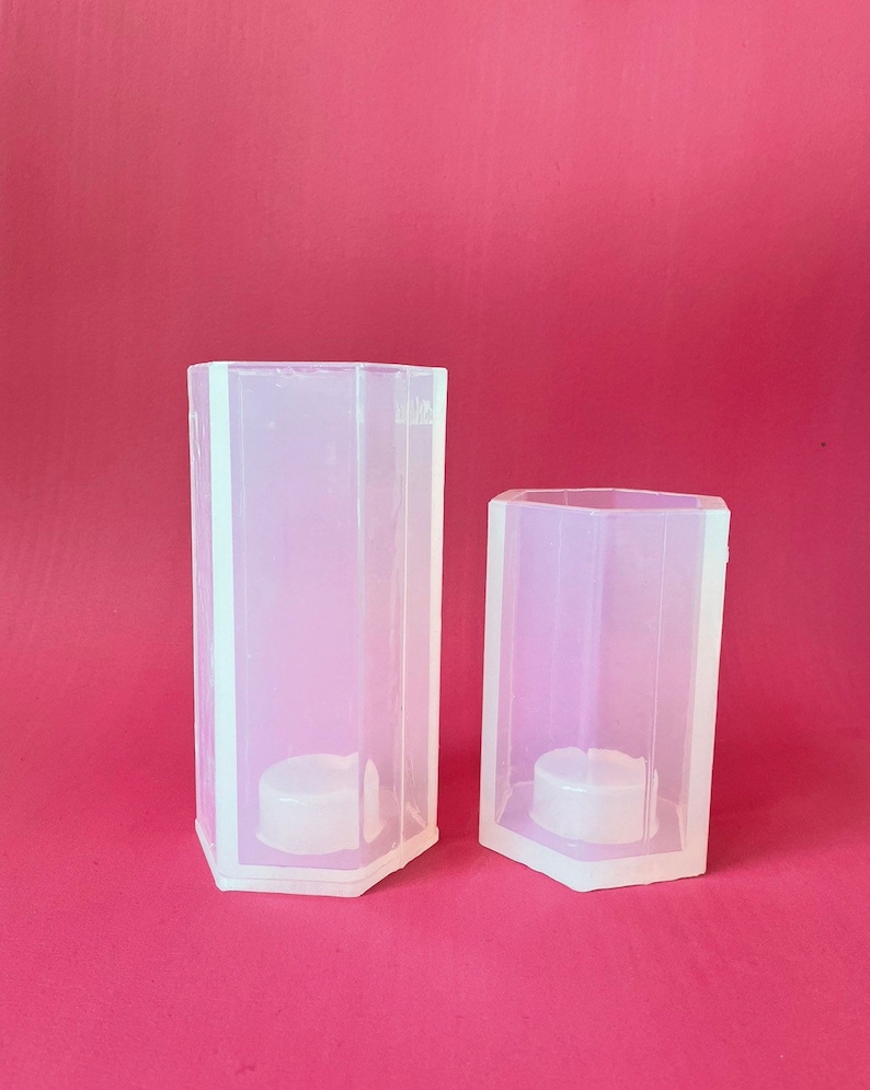 May include: Two clear plastic hexagonal candle molds. The larger mold is taller than the smaller mold.
