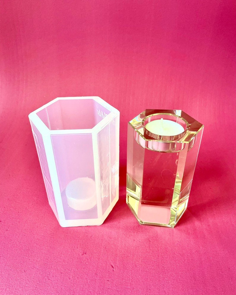 May include: A clear glass candle holder with a hexagonal shape and a white silicone mold for making candles. The candle holder is empty and the mold has a small white candle inside.