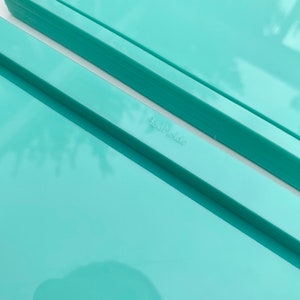 May include: Two turquoise plastic trays stacked on top of each other. The top tray has a slightly raised edge. The bottom tray has a slightly lower edge. The word "Handmade" is printed on the bottom tray.