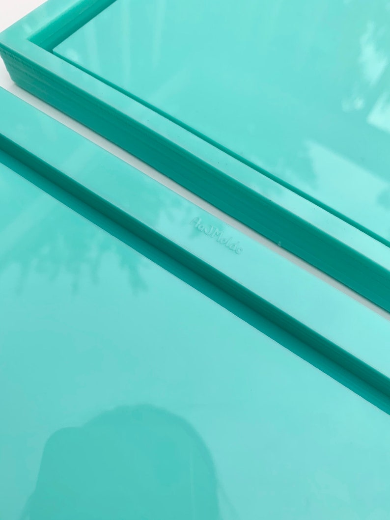 May include: Two turquoise plastic trays stacked on top of each other. The top tray has a slightly raised edge. The bottom tray has a slightly lower edge. The word "Handmade" is printed on the bottom tray.