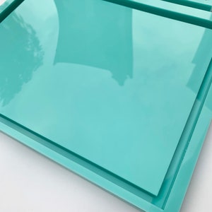 May include: A set of two teal rectangular trays with a raised edge. The trays are stacked on top of each other.
