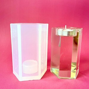 May include: A clear glass candle holder with a hexagonal shape and a silver metal top. Next to it is a clear silicone mold with the same shape.