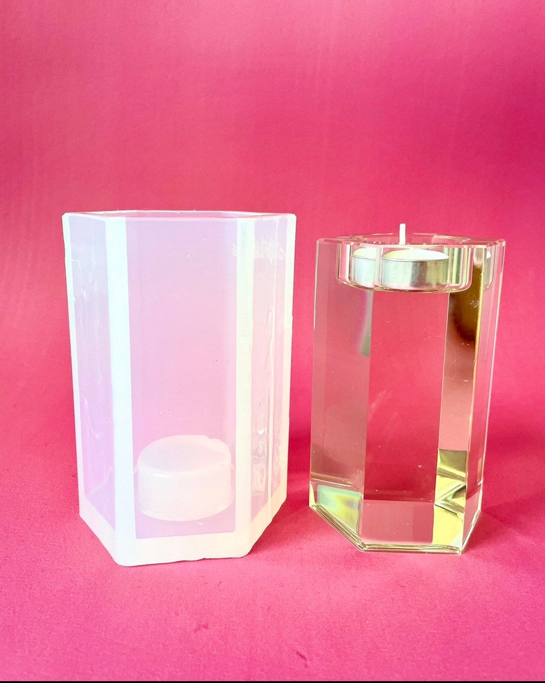 May include: A clear glass candle holder with a hexagonal shape and a silver metal top. Next to it is a clear silicone mold with the same shape.