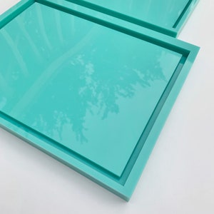 May include: Two turquoise square trays with a raised edge. The trays are stacked on top of each other.
