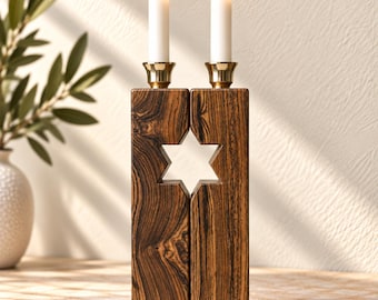 Puede incluir: Un candelabro rectangular de madera con un patrón de vetas de color marrón oscuro y un recorte en forma de Estrella de David en el centro. Dos copas de metal color latón están montadas arriba, cada una con una vela blanca larga y encendida.