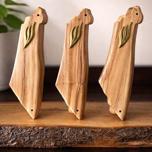 May include: Three handcrafted wooden sculptures with a light brown finish and a brass leaf accent. The sculptures are displayed on a wooden surface with a natural edge, showcasing the wood grain and texture.
