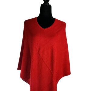 Op de afbeelding: Een effen rode poncho met een V-hals, gepresenteerd op een zwarte mannequin. De achtergrond is wit. De poncho is gemaakt van een zachte, soepele stof, ideaal om te dragen. Een veelzijdig kledingstuk.