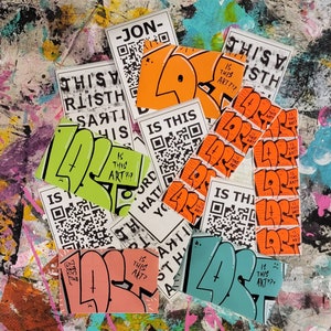 May include: A collection of colourful stickers with various designs and text, including "Is This Art?" and "This Is Art". The stickers are on a textured background.