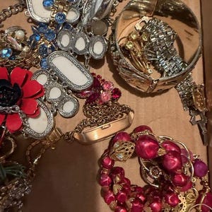 Pode incluir: Uma cole&ccedil;&atilde;o de joias vintage, incluindo colares, pulseiras e broches. As pe&ccedil;as apresentam v&aacute;rias cores, incluindo vermelho, azul e dourado. Alguns itens t&ecirc;m designs ornamentados com strass e p&eacute;rolas.