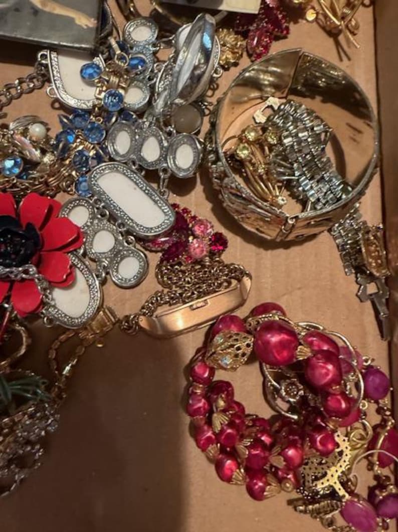 Pode incluir: Uma cole&ccedil;&atilde;o de joias vintage, incluindo colares, pulseiras e broches. As pe&ccedil;as apresentam v&aacute;rias cores, incluindo vermelho, azul e dourado. Alguns itens t&ecirc;m designs ornamentados com strass e p&eacute;rolas.