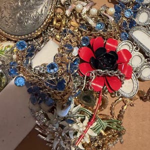 Pode incluir: Uma cole&ccedil;&atilde;o de joias vintage, incluindo colares, pulseiras e broches. As pe&ccedil;as apresentam v&aacute;rias cores, incluindo ouro, prata, vermelho e azul. Alguns itens t&ecirc;m pedras preciosas e p&eacute;rolas. Uma grande fivela de cinto prateada tamb&eacute;m &eacute; vis&iacute;vel.