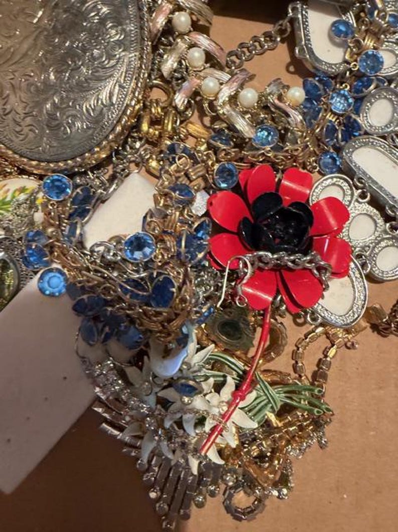 Pode incluir: Uma cole&ccedil;&atilde;o de joias vintage, incluindo colares, pulseiras e broches. As pe&ccedil;as apresentam v&aacute;rias cores, incluindo ouro, prata, vermelho e azul. Alguns itens t&ecirc;m pedras preciosas e p&eacute;rolas. Uma grande fivela de cinto prateada tamb&eacute;m &eacute; vis&iacute;vel.