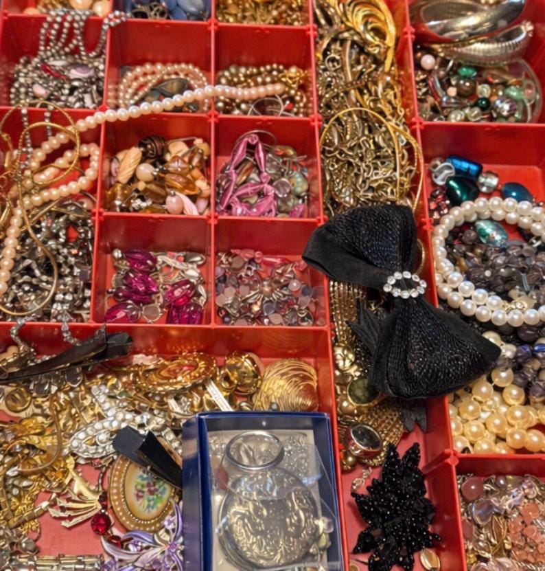 Pode incluir: Um organizador de joias vermelho dividido, cheio de v&aacute;rios colares, pulseiras, broches e brincos. As joias incluem pe&ccedil;as de ouro, prata, p&eacute;rolas e pedras preciosas. Uma fita preta com um centro de strass tamb&eacute;m &eacute; vis&iacute;vel.