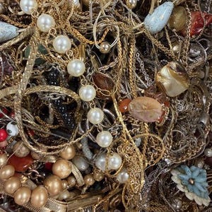 Pode incluir: Uma variedade emaranhada de joias vintage, incluindo colares, pulseiras e brincos dourados. A cole&ccedil;&atilde;o apresenta p&eacute;rolas, contas e v&aacute;rios estilos de pingentes. Uma mistura de texturas e cores cria um visual rico e em camadas.