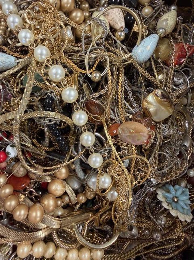 Pode incluir: Uma variedade emaranhada de joias vintage, incluindo colares, pulseiras e brincos dourados. A cole&ccedil;&atilde;o apresenta p&eacute;rolas, contas e v&aacute;rios estilos de pingentes. Uma mistura de texturas e cores cria um visual rico e em camadas.