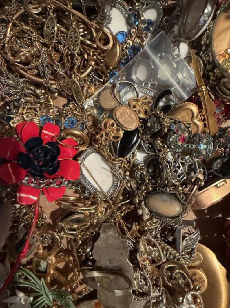 Pode incluir: Uma cole&ccedil;&atilde;o de joias vintage, incluindo colares, pulseiras, an&eacute;is e broches. As pe&ccedil;as s&atilde;o de v&aacute;rios estilos e cores, com tons dourados e prateados, e algumas com pedras preciosas e detalhes em esmalte. Uma broche de flor vermelha e preta &eacute; vis&iacute;vel.