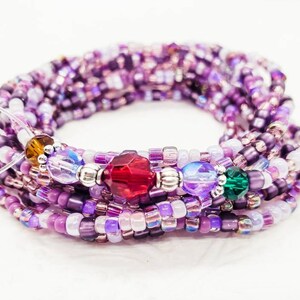 Peut inclure: Un bracelet en perles violettes et blanches avec des perles d'accent en cristal rouge, vert et clair.