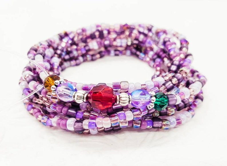 Peut inclure: Un bracelet en perles violettes et blanches avec des perles d'accent en cristal rouge, vert et clair.