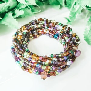 Peut inclure: Bracelet multicolore en perles avec un charme en cristal. Le bracelet est compos&eacute; de petites perles rondes dans des tons de brun, violet, vert et or. Le charme en cristal est de couleur violet fonc&eacute;.