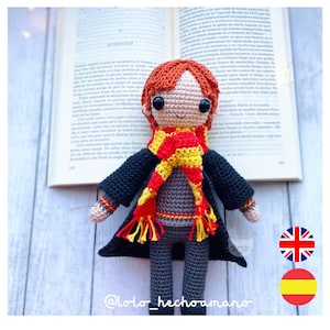 May include: Crocheted plush toy of a red-haired boy wearing a black robe, a red and yellow scarf, and grey pants. The toy is sitting on a book with the title "QUIDDITCH" visible.