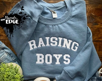 Peut inclure: Un sweat-shirt bleu avec du texte blanc qui dit "Raising Boys".