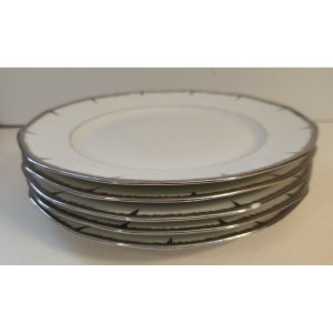May include: A stack of five white porcelain dinner plates with a silver rim and a subtle gray pattern.
