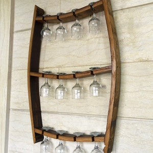 May include: A wooden wine glass rack made from a repurposed barrel stave. The rack has three tiers and can hold 12 wine glasses. The rack is mounted on a wall.