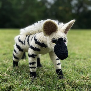 Op de afbeelding: Een gehaakt knuffeldier dat lijkt op een zebra met zwart-witte strepen. Het dier heeft een bruine neus en zwarte ogen.