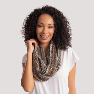 May include: A woman with curly brown hair is wearing a white t-shirt and a brown, grey, and yellow infinity scarf.