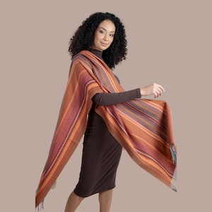 May include: A woman wearing a brown dress and a long, striped shawl with orange, pink, and purple stripes. The shawl has a fringe at the bottom.