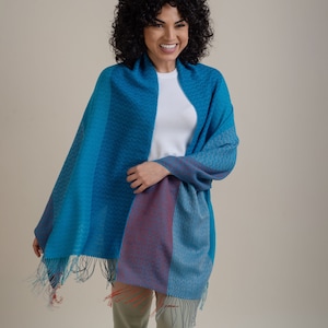 May include: A blue, red and white patterned scarf with fringe. The scarf is draped around a person's shoulders.