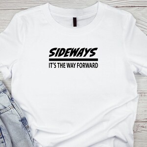 Puede incluir: Camiseta blanca con texto negro que dice "SIDEWAYS IT'S THE WAY FORWARD".