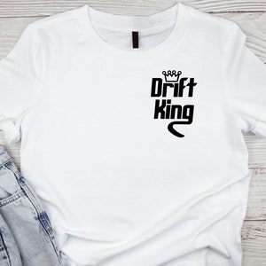 Puede incluir: Camiseta blanca con un gráfico negro que dice "Drift King" con una corona sobre la palabra "Drift".