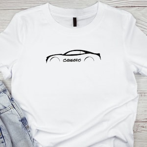 Puede incluir: Camiseta blanca con una silueta negra de un coche Camaro y la palabra "CAMARO" impresa debajo.