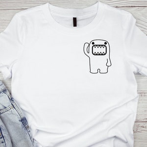 Puede incluir: Camiseta blanca con un contorno negro de un monstruo de dibujos animados con una gran boca y un brazo levantado.