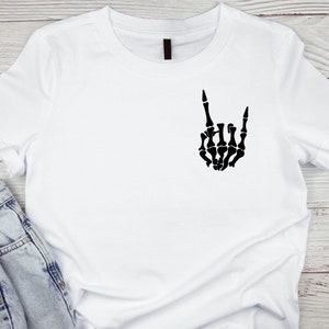 Puede incluir: Camiseta blanca con una mano de esqueleto negra haciendo el gesto de rock and roll.