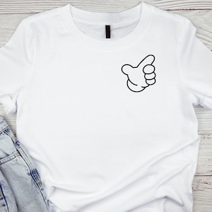 Puede incluir: Camiseta blanca con una mano de dibujos animados negra haciendo un gesto de pulgar hacia arriba.