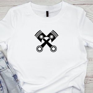 Puede incluir: Camiseta blanca con un gráfico negro de dos pistones de motor cruzados.