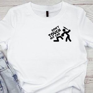 Puede incluir: Camiseta blanca con un gráfico negro que dice "Don't Touch My Car" y un figurín con un arma.