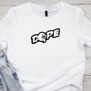 Puede incluir: Camiseta blanca con un gráfico negro de un fantasma con la lengua afuera y la palabra "DOPE" en letras negritas.