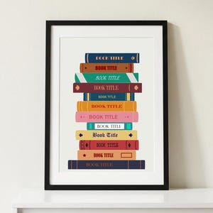 May include: A framed wall art print featuring a vertical stack of eleven colorful books. Each book spine is a different solid color, including blue, orange, green, maroon, yellow, pink, and dark navy, all with the text BOOK TITLE printed on them.