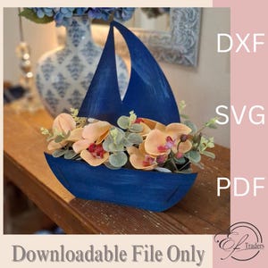 Puede incluir: Un macetero de madera azul en forma de velero con un arreglo floral de orquídeas melocotón y blancas y eucalipto. El macetero está sentado en una mesa de madera. La imagen incluye el texto "DXF SVG PDF Downloadable File Only"