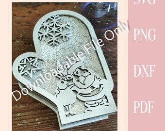 May include: A silver glitter-covered wooden mitten with a cut-out design of a snowman and snowflake. The mitten is a 3D box.