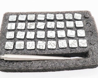Könnte beinhalten: Ein Satz mit 48 Stempeln aus Metall mit verschiedenen Designs, darunter Schmetterlinge, Blumen und geometrische Formen. Die Stempel sind in einem Raster angeordnet und werden mit einem Metallgriff geliefert.