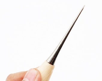 May include: A close-up of a hand holding a wooden and metal awl with a sharp point. The awl is used for leather crafting and sewing.